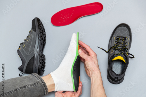 Close up of man hands fitting orthopedic insoles on a gray background.