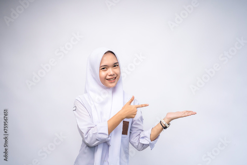 Excited Female Indonesian high school student in white and grey uniform, pointing at the copy space beside her, isolated by white background