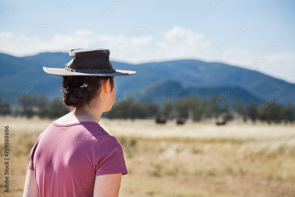 A teen farm kid in an akubra hat standing in farm paddock A teen farm kid in an akubra hat standing in farm paddock