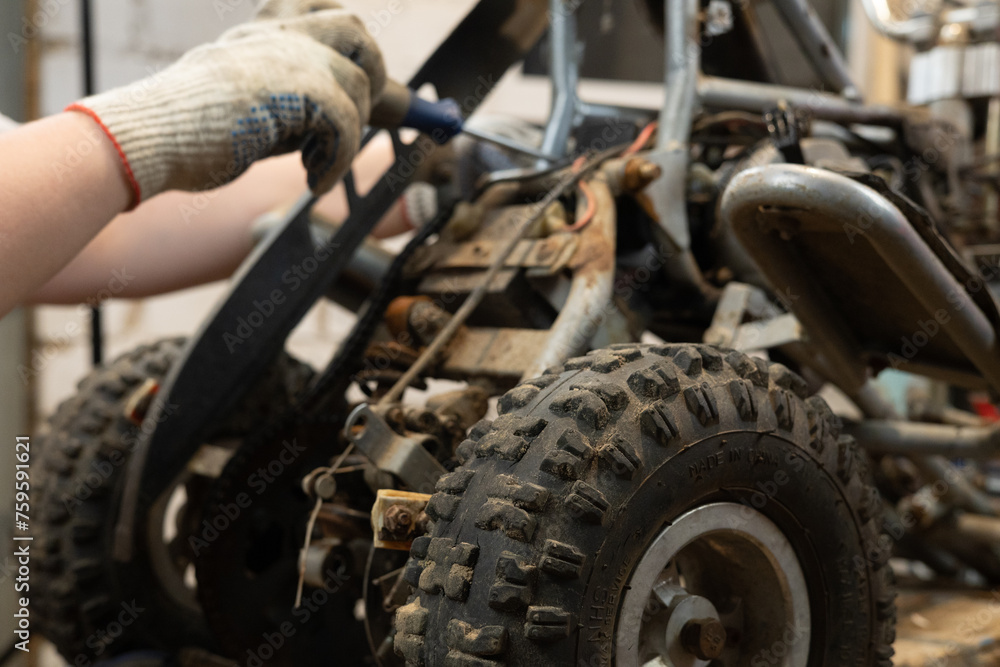A male mechanic replaces a broken part in his son's ATV with a new one using tools. A man is repairing a small children's ATV in a garage near his house. ATV repair concept. A male mechanic replaces a broken part in his son's ATV with a new one using tools. A man is repairing a small children's ATV in a garage near his house. ATV repair concept.