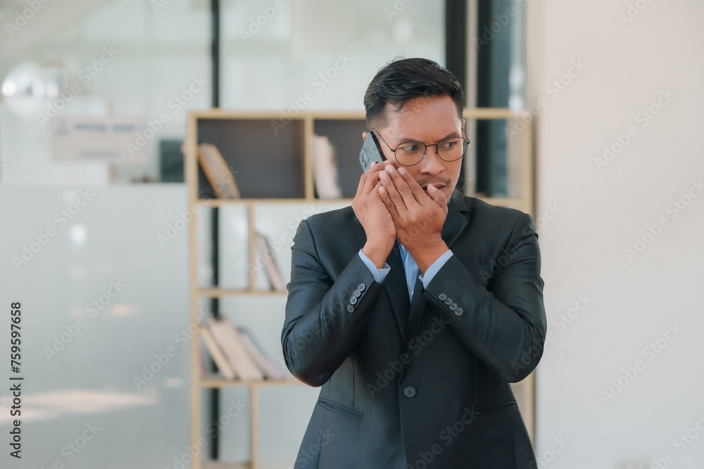 Asian businessman in a suit is talking on his cell phone in the office. Asian businessman in a suit is talking on his cell phone in the office.