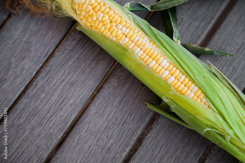 Sweet corn with green husk on wooden table background