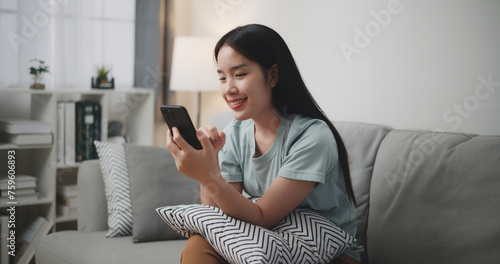 Happy young woman sitting on sofa enjoy using mobile phone for online shopping cashless in living room at home, Technology money wallet and Online payment concept
