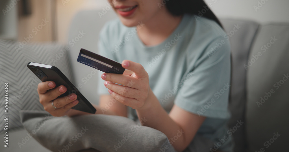 Selective focus, Hands of Young asian woman sitting on sofa holding credit card making online payment for purchase in web store using smartphone. Selective focus, Hands of Young asian woman sitting on sofa holding credit card making online payment for purchase in web store using smartphone.