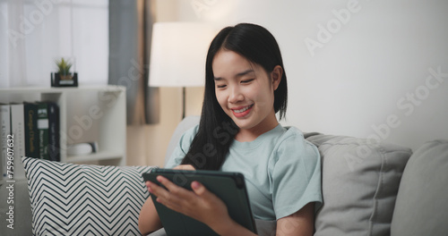 Selective focus, Happy young woman sitting on sofa using digital tablet for online shopping cashless in living room at home,