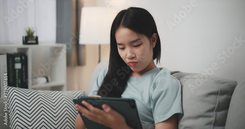 Selective focus, Happy young woman sitting on sofa using digital tablet for online shopping cashless in living room at home