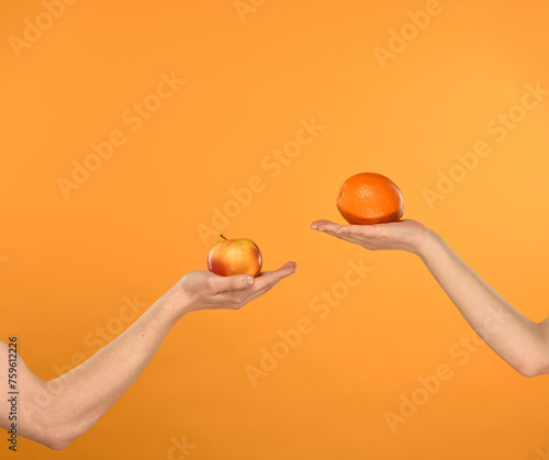 hands showing red yellow apple and orange on orange background with free space for text