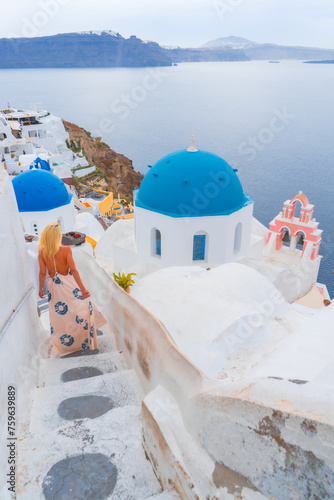 woman model is walking strrets of Oia town on Santorini island in Greece. Travel mediterranean aegean of traditional cycladic Santorini white houses and blue dome