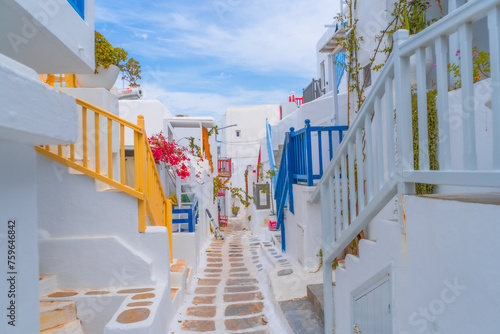 Fototapeta Naklejka Na Ścianę i Meble -  narrow side street with traditional whitewashed walls and blue accents in Mykanos Greece. traditional windmill on the sea shore and colorful restaurants