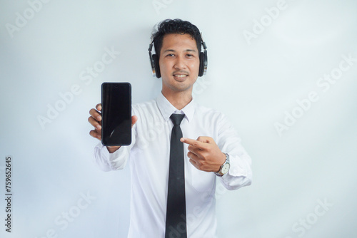 Adult Asian man smiling confident while pointing finger to blank handphone screen. using headphone photo