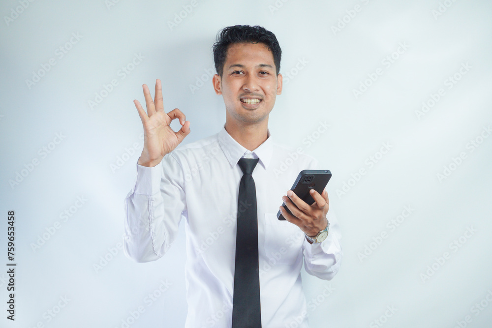 Adult Asian man smiling confident and give OK finger sign while holding a mobile phone Adult Asian man smiling confident and give OK finger sign while holding a mobile phone