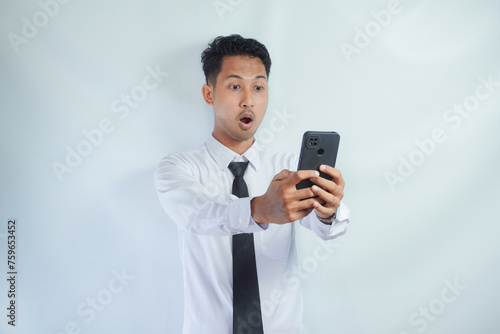 Adult Asian man looking to mobile phone that he hold with surprised expression photo