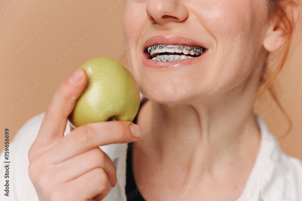 Portrait of mature woman with braces on teeth eating green apple on beige background Portrait of mature woman with braces on teeth eating green apple on beige background