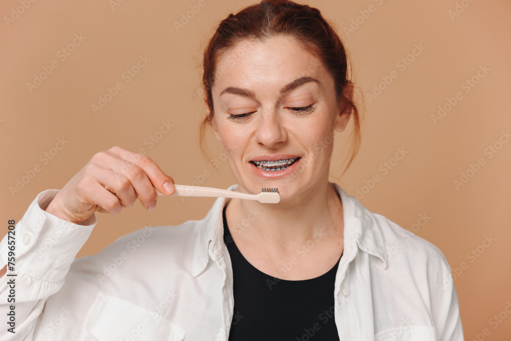Happy mature woman in braces holding a toothbrush on a beige background Happy mature woman in braces holding a toothbrush on a beige background