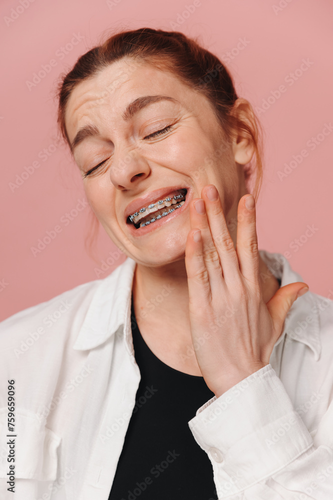 Portrait of red-haired mature woman suffering from pain due to braces on pink background Portrait of red-haired mature woman suffering from pain due to braces on pink background