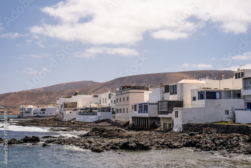 Seascape. Arrieta village pier with typical white houses, mountains in the background. Turquoise Atlantic Ocean. Big white clouds. Village of Arrieta. Lanzarote, Canary Islands, Spain photo