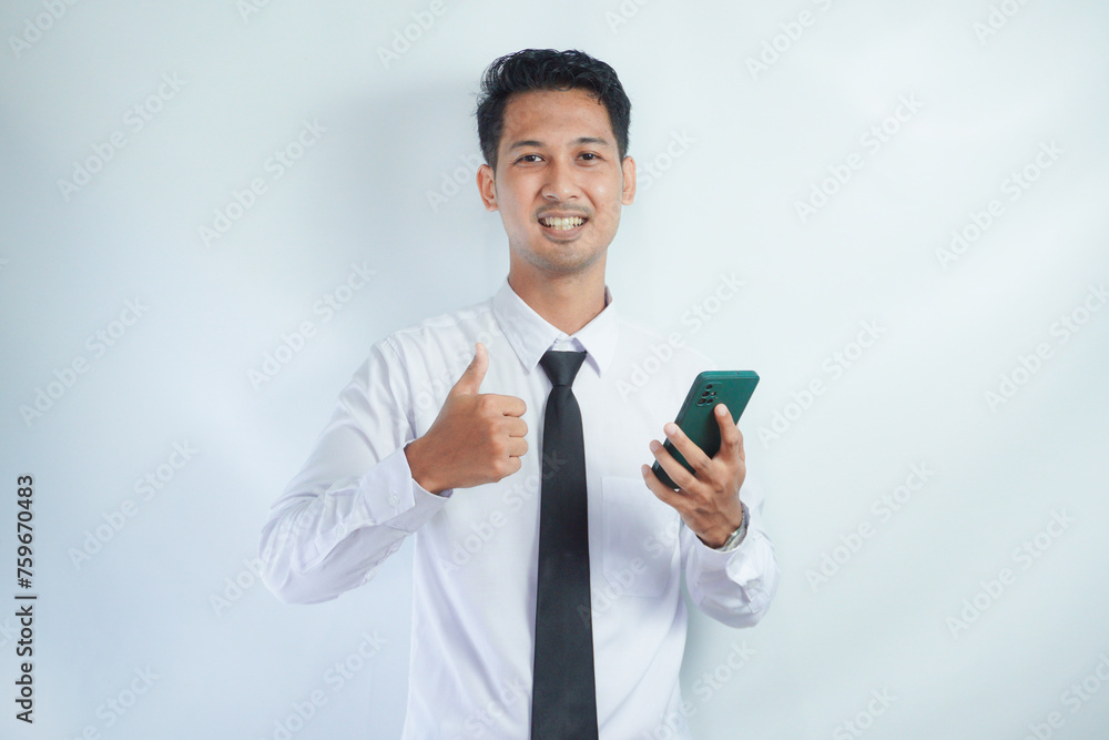 Adult Asian man wearing white shirt and tie smiling and give thumb up while holding mobile phone Adult Asian man wearing white shirt and tie smiling and give thumb up while holding mobile phone