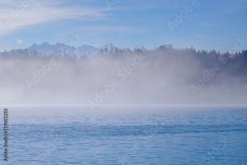 Mountain landscape.. In the foreground, Lake Czorsztynskie and fog rising from the water. View of the Tatra Mountains from the Pieniny Mountain Range. Poland.