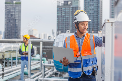 Man engineer holding laptop working at rooftop building construction. Male technician worker working checking hvac of office building. Engineering installing large air conditioning system. photo