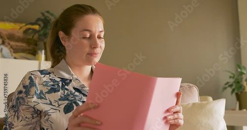 a woman is reading a book at home on a sofa in the beautiful daylight.