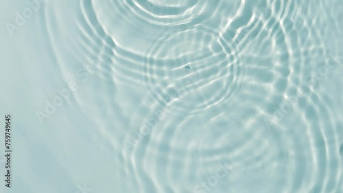 transparent blue slow motion water wave circles with rain drops from above, sunny pure water texture background for beauty care, spa and cosmetics