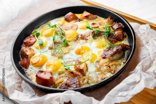 Close-up view of a hearty skillet breakfast with sunny side up eggs, cooked sausages, and fresh herbs, served on a wooden tray. Perfect for a delicious start to the day