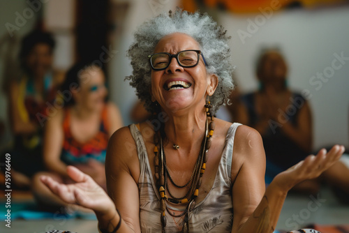 A person participating in a laughter yoga class to boost mood and relieve stress. An older woman is sitting on the floor with her arms outstretched and laughing among other people © ivlianna