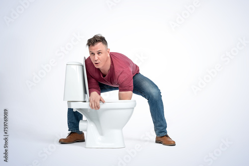 A man in casual clothes put his hand in the toilet and felt something there, on a light blue background