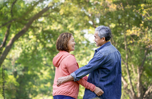 rear view of romantic senior couple looking each other and smile while taking a walk in nature in the park,concept health benefits of nature in elderly and family relationship