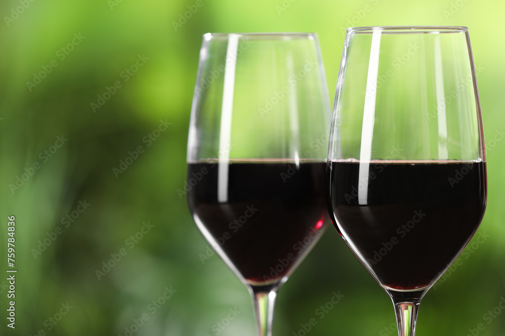 Tasty red wine in glasses against blurred green background, space for text Tasty red wine in glasses against blurred green background, space for text