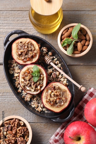 Tasty baked apples with nuts, honey and mint in baking dish on wooden table, flat lay