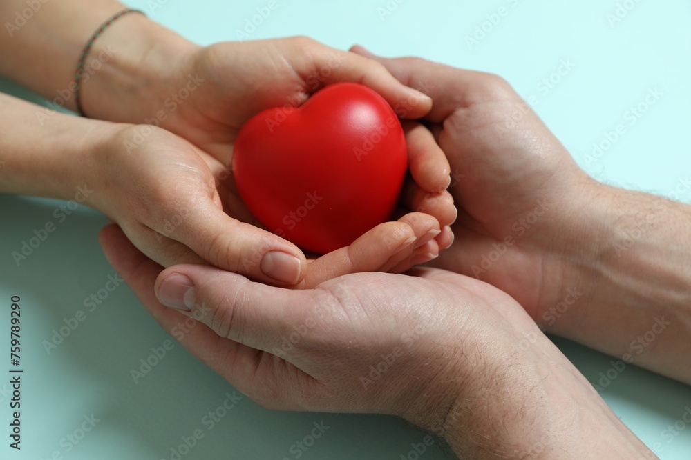 Fototapeta premium Couple holding red decorative heart on light blue background, closeup