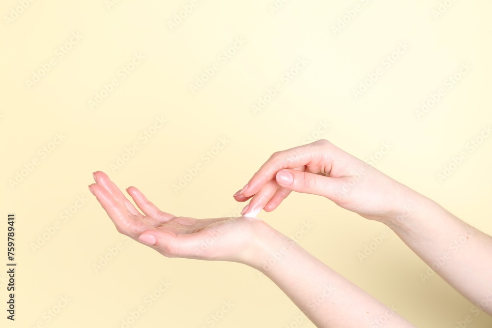 Woman applying cream on her hand against yellow background, closeup