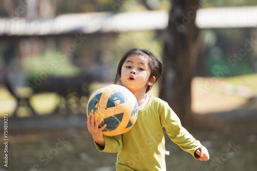 A young girl is holding a soccer ball in her hands. She is wearing a green shirt and she is excited about playing soccer