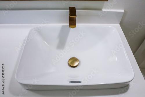 Close up of a white porcelain sink in a bathroom with brushed gold fixtures