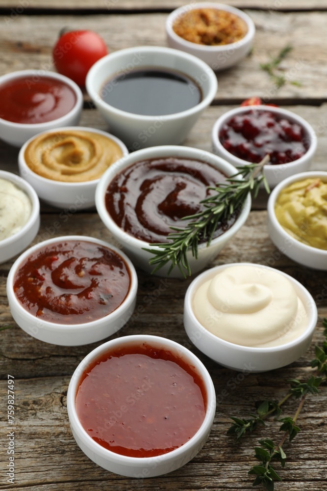 Different tasty sauces in bowls, rosemary and thyme on wooden table Different tasty sauces in bowls, rosemary and thyme on wooden table