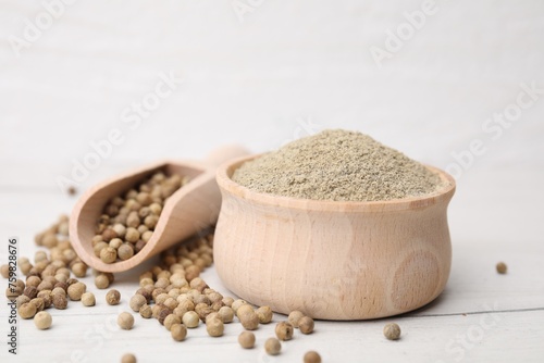 Aromatic spice. Ground pepper in bowl and scoop with peppercorns on white wooden table, closeup