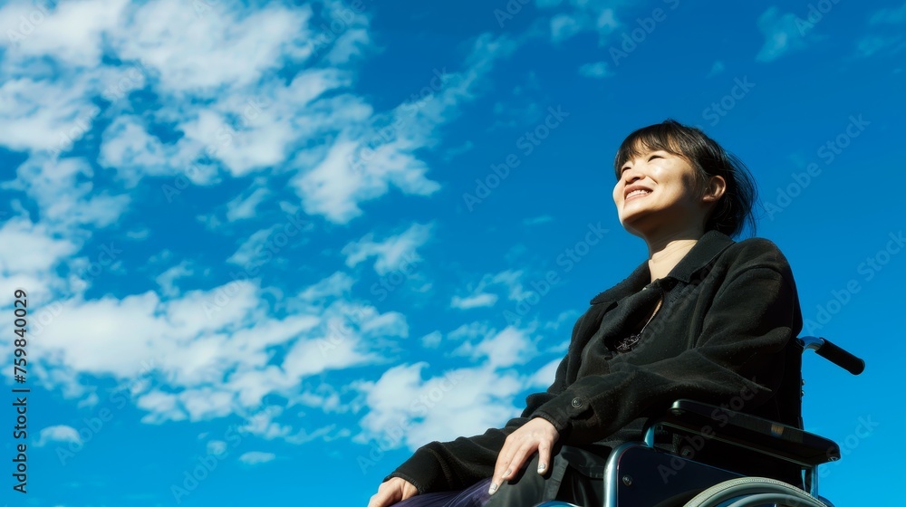 Japanese woman in a wheelchair smiling with a blue sky with clouds in the background in a low angle shot Japanese woman in a wheelchair smiling with a blue sky with clouds in the background in a low angle shot