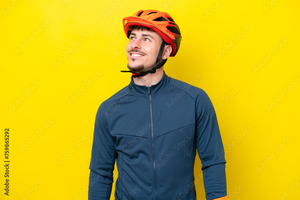 Fototapeta premium Young cyclist caucasian man isolated on yellow background thinking an idea while looking up