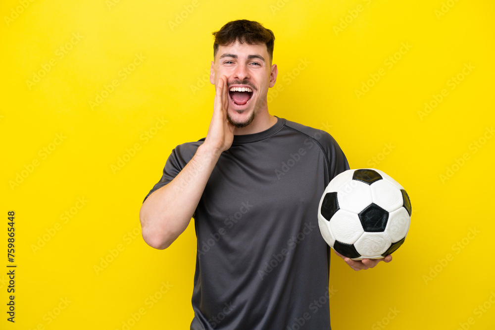 Young football player man isolated on yellow background shouting with mouth wide open Young football player man isolated on yellow background shouting with mouth wide open