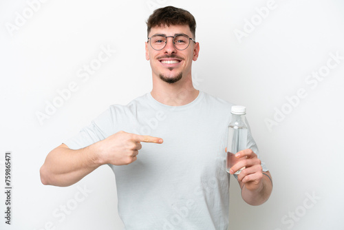 Young caucasian man holding a bottle of water isolated on white background and pointing it