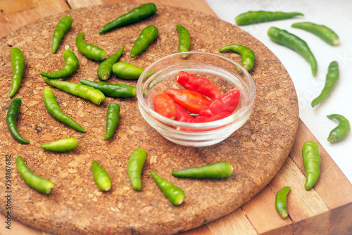 Raw red chilli in glass bowl with green chillies in a surrounding at wooden board (ID: 759867682)