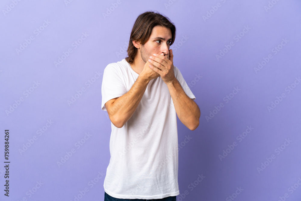 Young handsome man isolated on purple background covering mouth and looking to the side Young handsome man isolated on purple background covering mouth and looking to the side