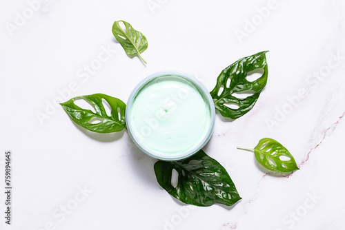 Organic eco friendly anticellulite cream with fresh decorative monstera leaves on white marble background top view.