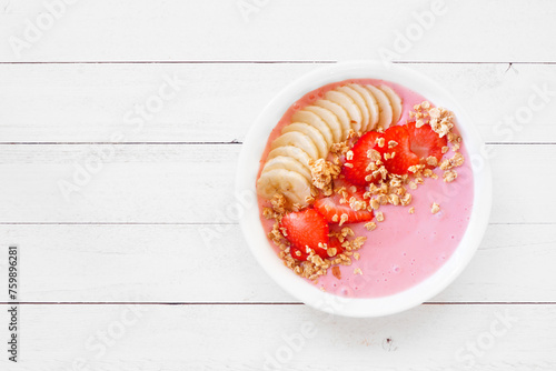 Healthy strawberry and banana smoothie bowl with granola. Top view on a white wood background.