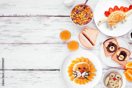 Fun child theme breakfast side border with a variety of animal themed food. Top down view on a white wood background. Pancakes, oatmeal, toast, fruit and cereal.