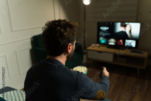 Rear view of an hispanic man enjoying watching tv using streaming service