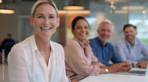 A group of professional individuals with beaming smiles are seated at a table  engaging in a collaborative meeting in a well-lit office space.