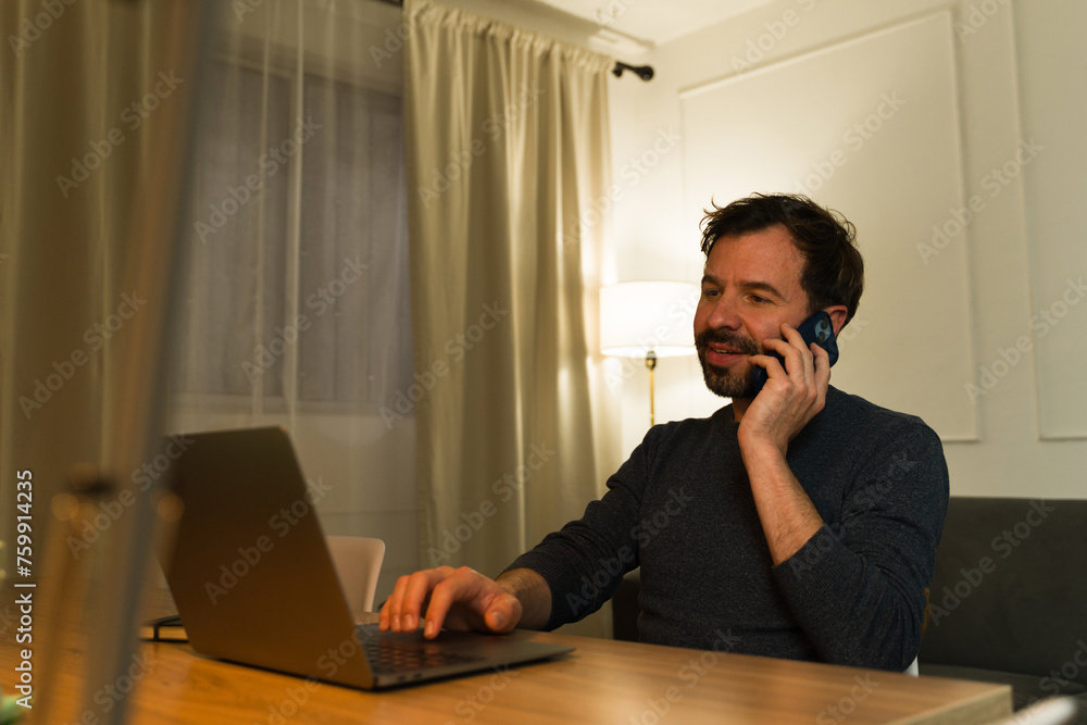 Attractive man working from home using the laptop talking on the phone