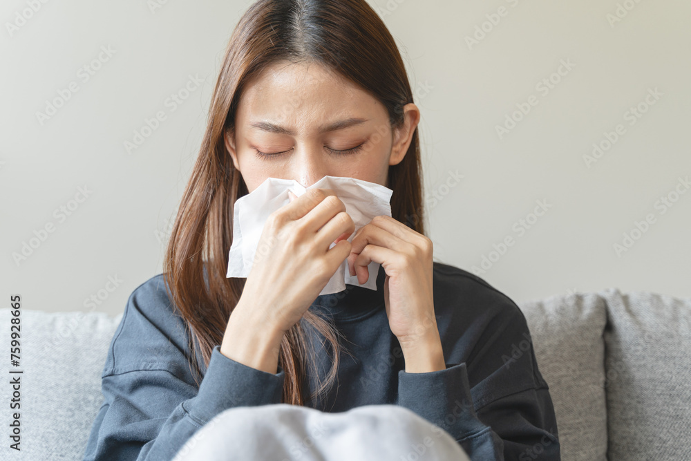 Sick at home concept. Woman sneezing on the sofa in winter season. - obrazy, fototapety, plakaty 
